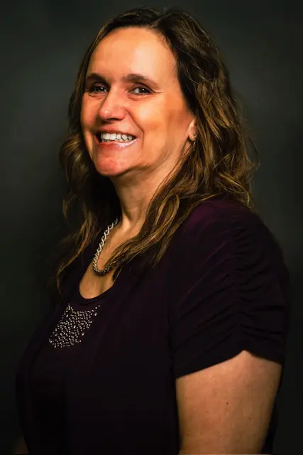 Smiling middle-aged woman with curly hair in a dark purple top.