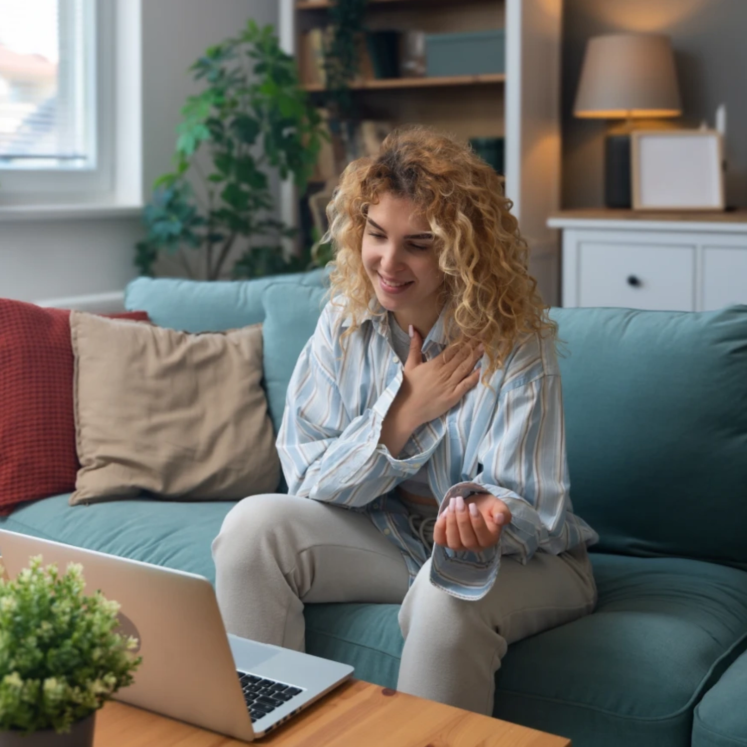 Woman sitting on couch using laptop and waving.