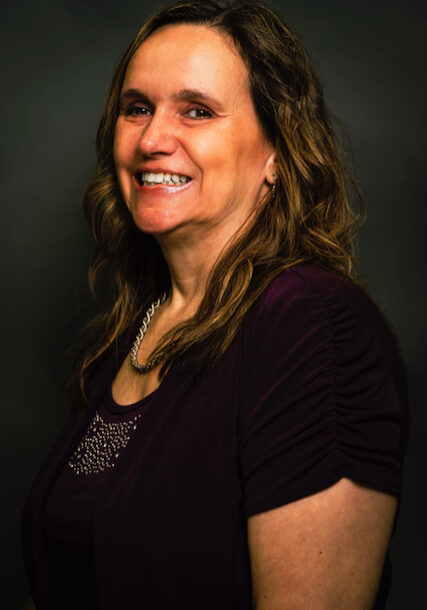 Smiling middle-aged woman with curly hair in a dark purple top.